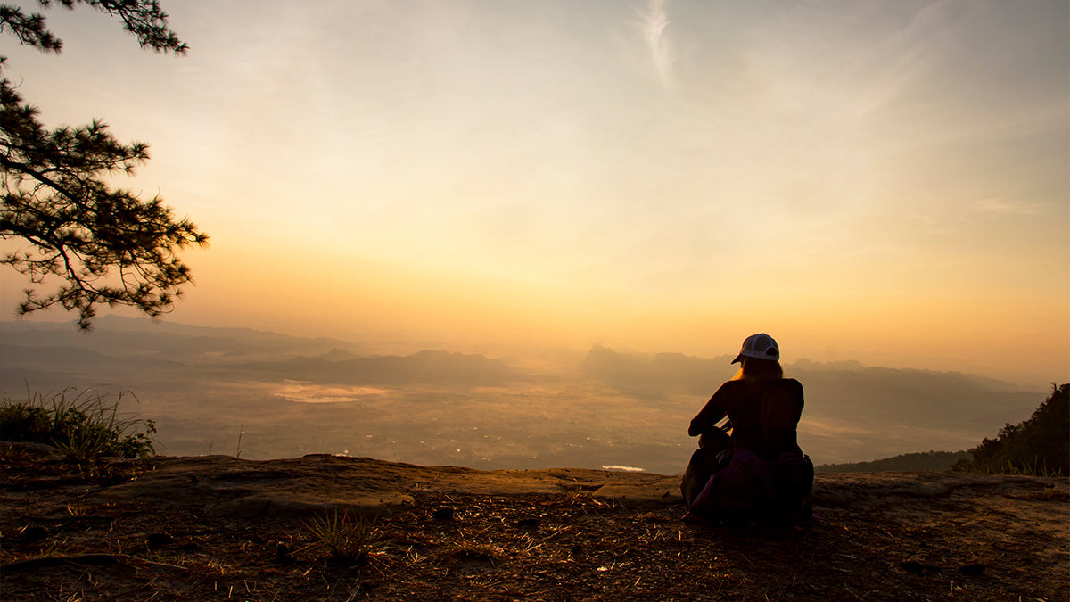 A person standing in an open valley, watching a sunset.