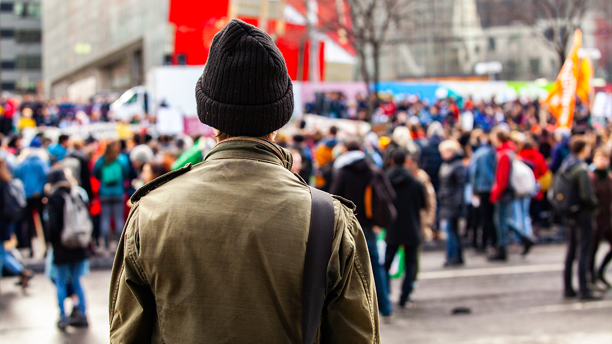 The back of an individual facing a large crowd of people in a busy city.