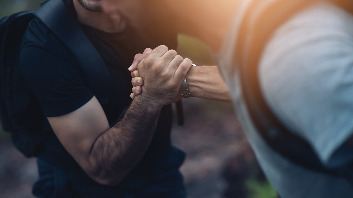 Two men in outdoor gear, gripping hands.