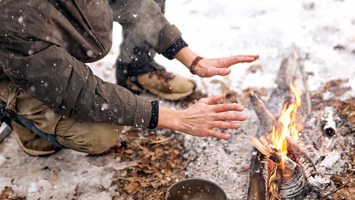 Man holding his hands to a fire in the snow.