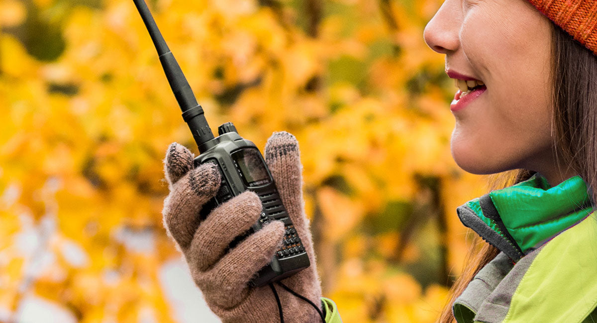 A woman holding a walkie-talkie radio in the wilderness.