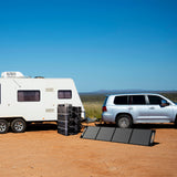 A robust solar power setup featuring a 'power tower' with seven 2200XP batteries connected to a central 2200 battery, arrayed neatly in front of a pull-behind camper, accompanied by an expansive solar panel array poised to harness solar energy, epitomizing a self-reliant, eco-friendly energy solution for mobile living.