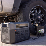 A 2200 battery is connected to a device under a car, depicting a roadside emergency or automotive maintenance scenario utilizing portable power.